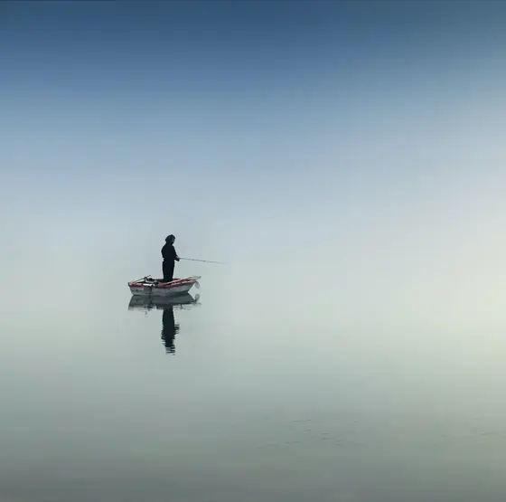 Ein Mensch steht allein in einem Boot auf einem stillen, nebligen See